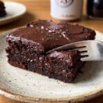 Close-up of a fork cutting into a moist Dr Pepper brownie with chocolate frosting.