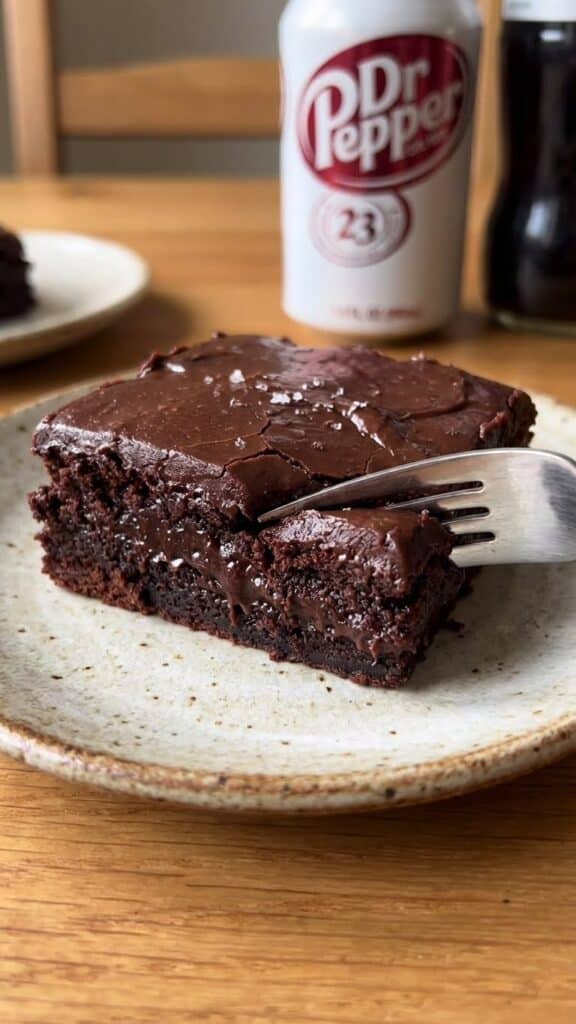 Close-up of a fork cutting into a moist Dr Pepper brownie with chocolate frosting.