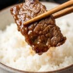 Close-up of chopsticks holding a piece of glistening soy-marinated beef.