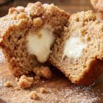 Close-up of a cinnamon muffin cut open to show the gooey cream cheese filling inside.