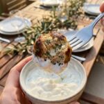 A close-up POV shot of a fork holding a bitten Greek chicken meatball dipped in tzatziki sauce, showing the herby interior.
