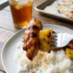 A close-up POV shot of a fork lifting a bite of glazed chicken and roasted pineapple over a bed of white rice.