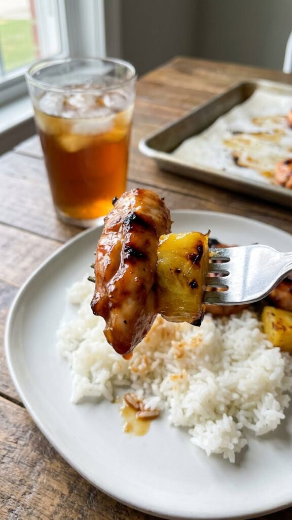 A close-up POV shot of a fork lifting a bite of glazed chicken and roasted pineapple over a bed of white rice.