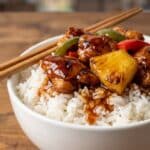 Close-up of a bowl of white rice topped with glazed Hawaiian chicken and pineapple.