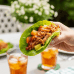 A hand holding a loaded Hawaiian pulled pork lettuce wrap outdoors on a sunny patio, ready to eat.