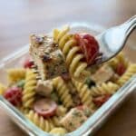 Close-up of a forkful of creamy chicken and pasta salad with a meal prep container in the background.