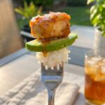 A close-up POV shot of a fork taking a bite from the stack, showing chicken, avocado, and rice together.