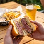 A person holding a halved cheeseburger showing a juicy medium-well interior.