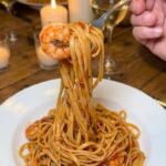 A close-up POV shot of a fork twirling linguine and a shrimp, coated in lemon garlic sauce.