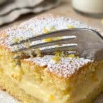 Close-up of a fork cutting into the soft custard layer of a lemon cake.