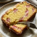 Close-up of a slice of lemon rhubarb loaf showing the moist texture and pink fruit inside.