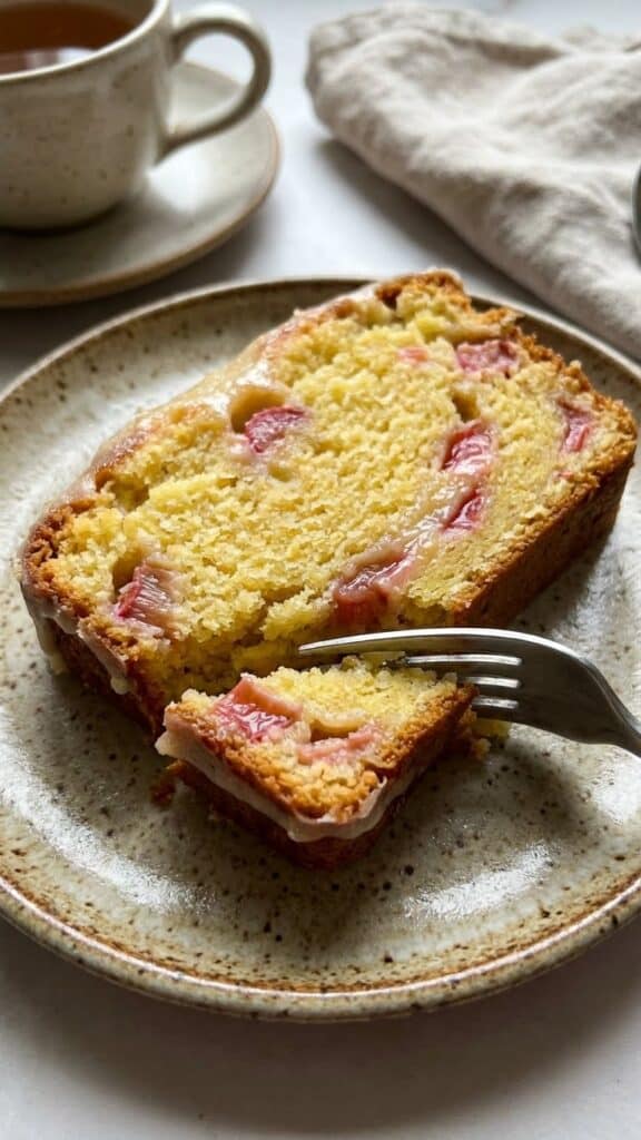Close-up of a slice of lemon rhubarb loaf showing the moist texture and pink fruit inside.