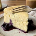 Close-up of a fork cutting into a slice of airy lemon soufflé cheesecake.