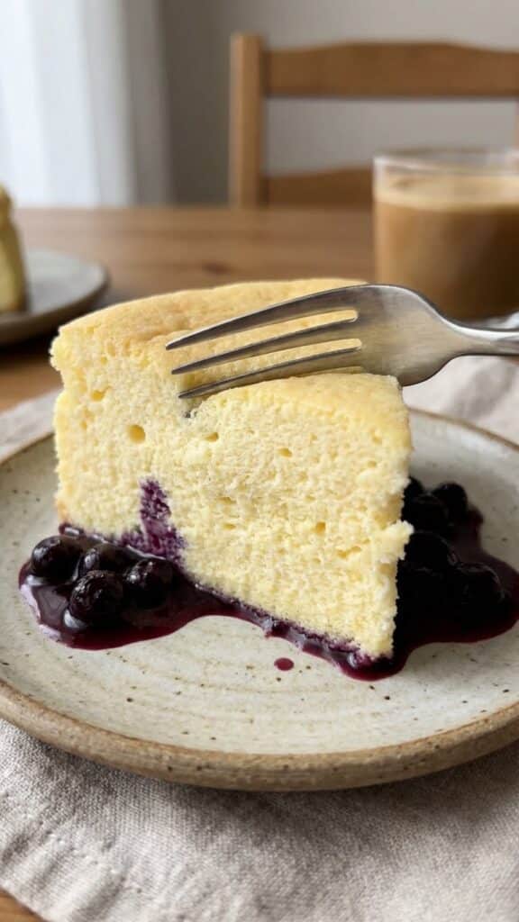 Close-up of a fork cutting into a slice of airy lemon soufflé cheesecake.