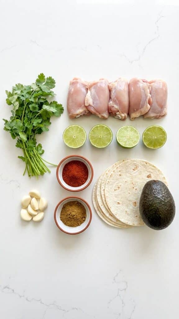 Flat lay of ingredients for lime chicken tacos including fresh limes, raw chicken, cilantro, and tortillas.