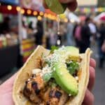 Close-up of a hand holding a chicken taco with lime juice dripping onto it.