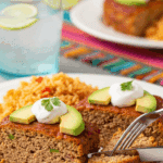 Plated slices of Mexican turkey meatloaf served with avocado, sour cream, and Spanish rice on a dinner table.