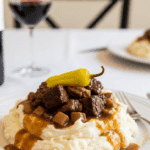 Plated Mississippi Roast served over creamy mashed potatoes with gravy and a pepper garnish.