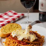 Plated Chicken Parmesan served over spaghetti with garlic bread and a glass of red wine.