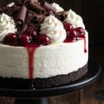 A close-up of a slice of No Bake Black Forest Cheesecake on a plate with a fork taking a bite, showing the creamy texture and cherry topping.
