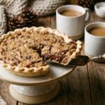A whole German chocolate pie on a cake stand with a slice being served.