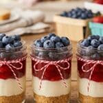 Individual patriotic cheesecakes served in mason jars with layered fruit.