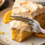 Close-up of a fork cutting into a fluffy slice of orange and vanilla cake.