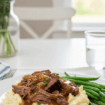 Plated Pot Roast served over creamy mashed potatoes with green beans on a bright table.