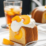 A slice of Peach Buttermilk Pound Cake served with whipped cream and fresh peaches on a patio table.