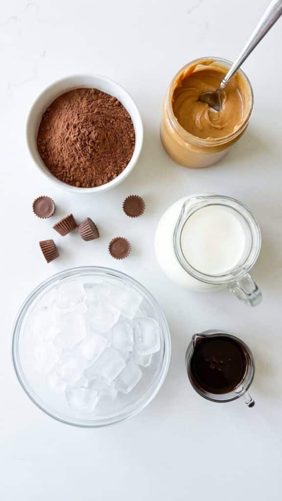 Overhead flat lay view of ingredients for frozen hot chocolate including cocoa powder, peanut butter, milk, ice, and chocolate sauce.