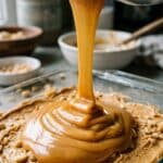 Pouring melted caramel over the peanut butter layer in a baking pan.