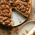 Overhead shot of a whole pecan pie with a slice missing revealing cheesecake.