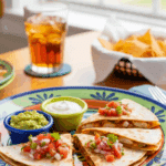 Plated chicken quesadilla wedges served with guacamole and sour cream on a sunny table.