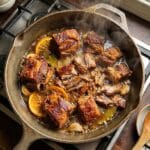 A sunny outdoor taco bar setup with a large bowl of pork carnitas surrounded by various toppings, tortillas, and hands building tacos.