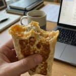 A hand holding a toasted chicken wrap with a bite taken out, showing the creamy filling.