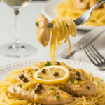 A plate of chicken piccata served over angel hair pasta, with a fork lifting a bite of chicken and noodles, set in an elegant dinner atmosphere.