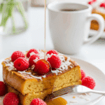 A plate of warm raspberry coconut French toast with syrup being poured over it, set on a sunny breakfast table with coffee.