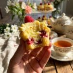 A hand holding a bitten lemon raspberry cupcake showing the fluffy texture and fruit inside.