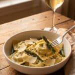 A bowl of asparagus and tomato ravioli served with white wine.
