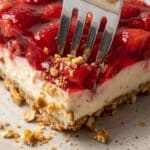 Close-up of a fork breaking through the pretzel crust of a strawberry dessert.