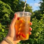 A hand holding a cold chocolate frappuccino drink outdoors on a sunny day.