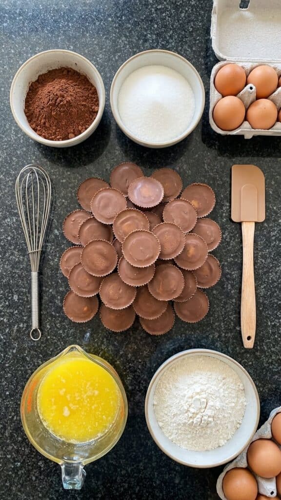 Overhead flat lay view of brownie ingredients centered around a large pile of unwrapped Reese's Peanut Butter Cups.