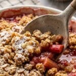 Close-up of a spoon lifting a portion of rhubarb crisp showing the fruit and topping layers.