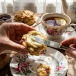 A glazed rhubarb scone served on a floral plate with a cup of tea in the background.