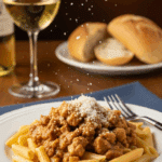 A plate of penne pasta topped with slow-cooked Italian chicken and peppers, sprinkled with parmesan cheese, served with white wine.