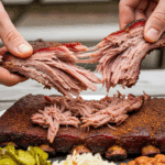 Hands pulling apart a tender Memphis-style dry rub rib, revealing shredded meat, served on a plate with coleslaw and beans outdoors.