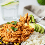 A burrito bowl filled with rice, beans, corn, and salsa chicken, with a fork lifting a bite of chicken and avocado.