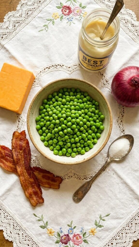 Ingredients for pea salad including green peas, cheddar block, bacon, red onion, and mayonnaise