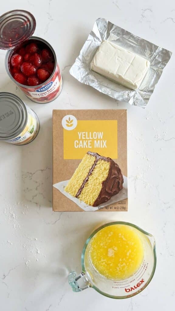 Ingredients for strawberry dump cake including cake mix, pie filling, cream cheese, and butter.