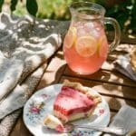 A slice of creamy strawberry pie served on a patio table with lemonade in the background.